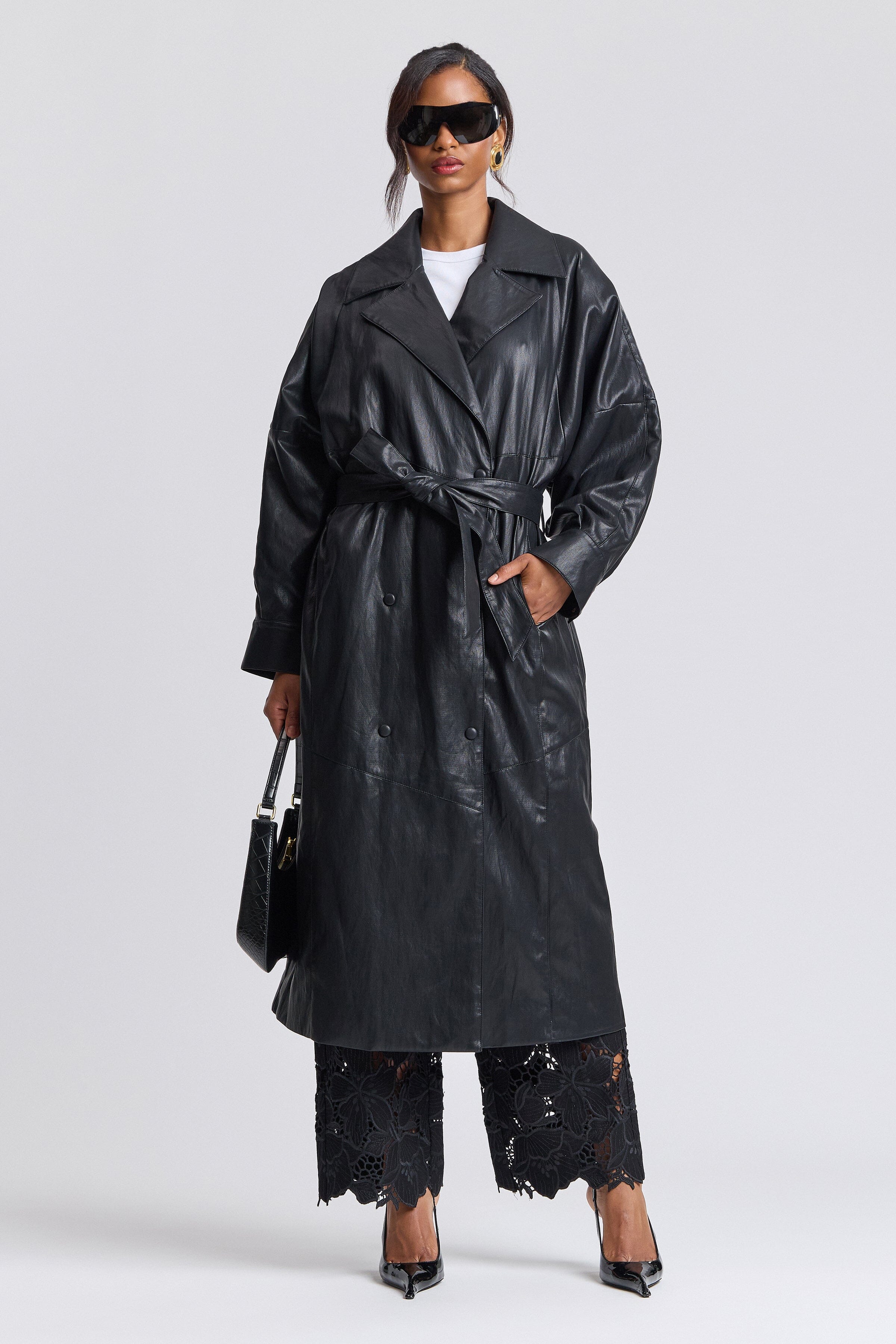 Double-breasted button-front black faux leather trench coat with point collar and adjustable belt by Avec Les Filles.