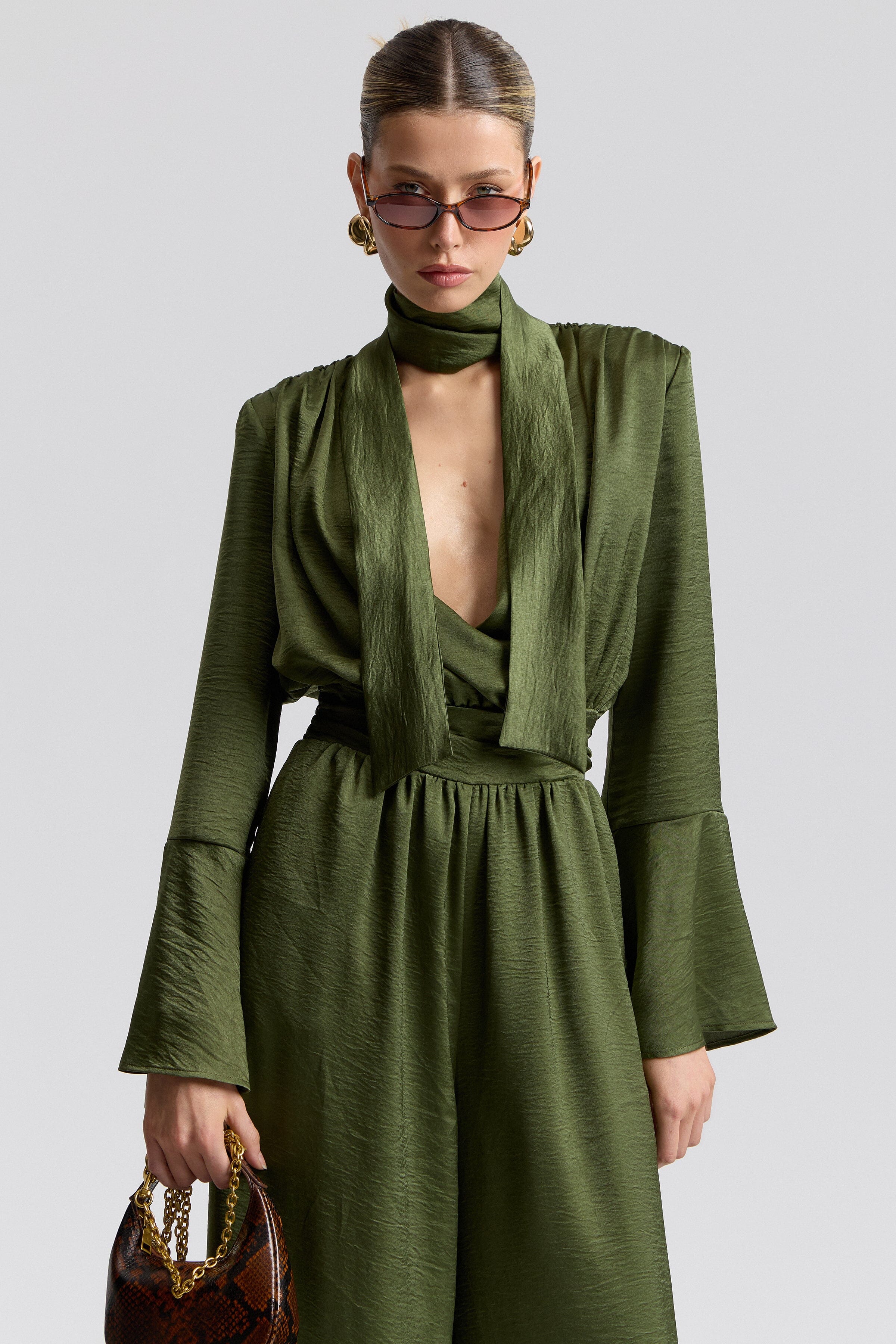 Tie-neck green satin jumpsuit with high neck, long slim sleeves and structured square shoulders by Avec Les Filles.