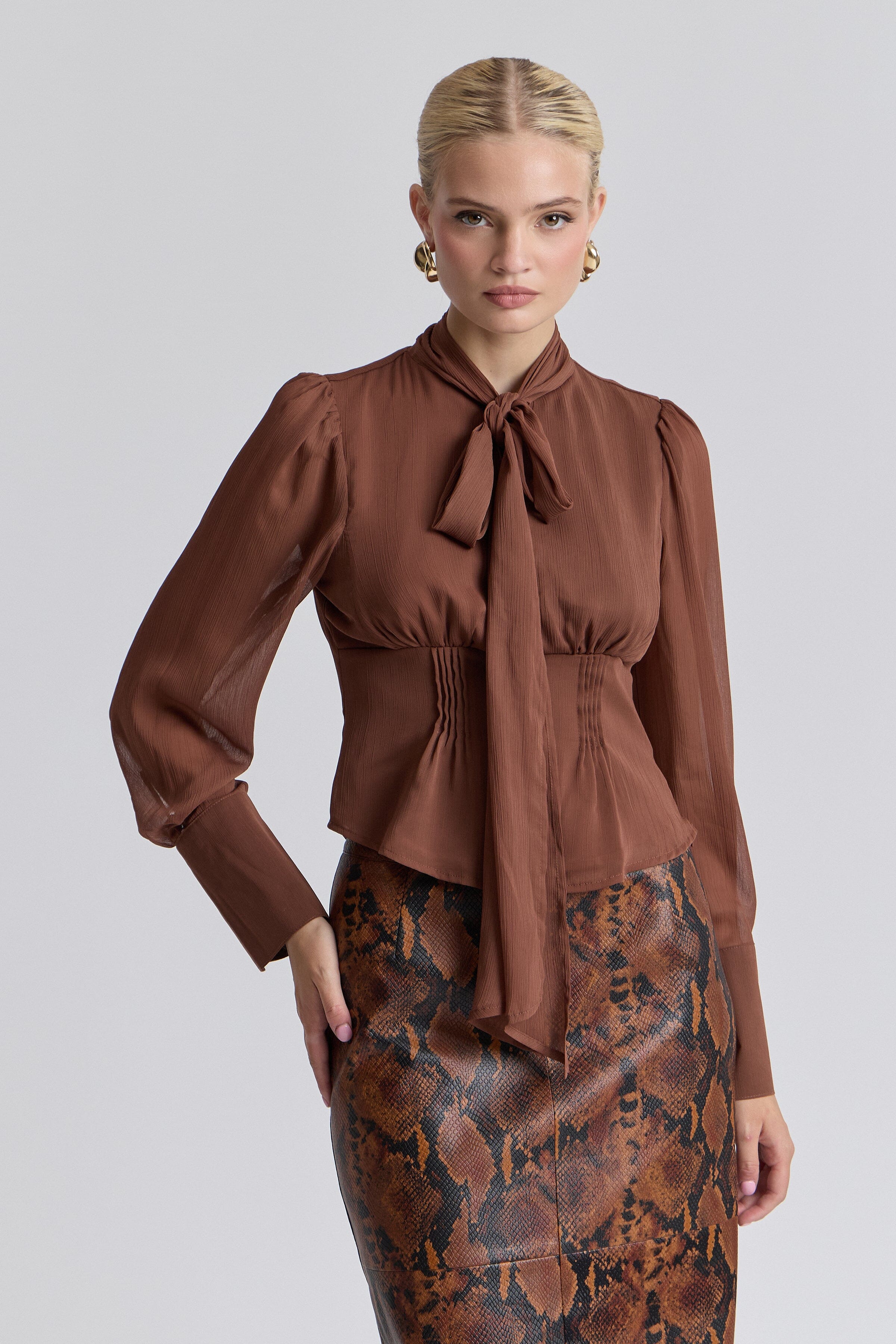 Brown chiffon tie-neck blouse with long puff sleeves and a faux-button front. Shop women's cute tops by Avec Les Filles.