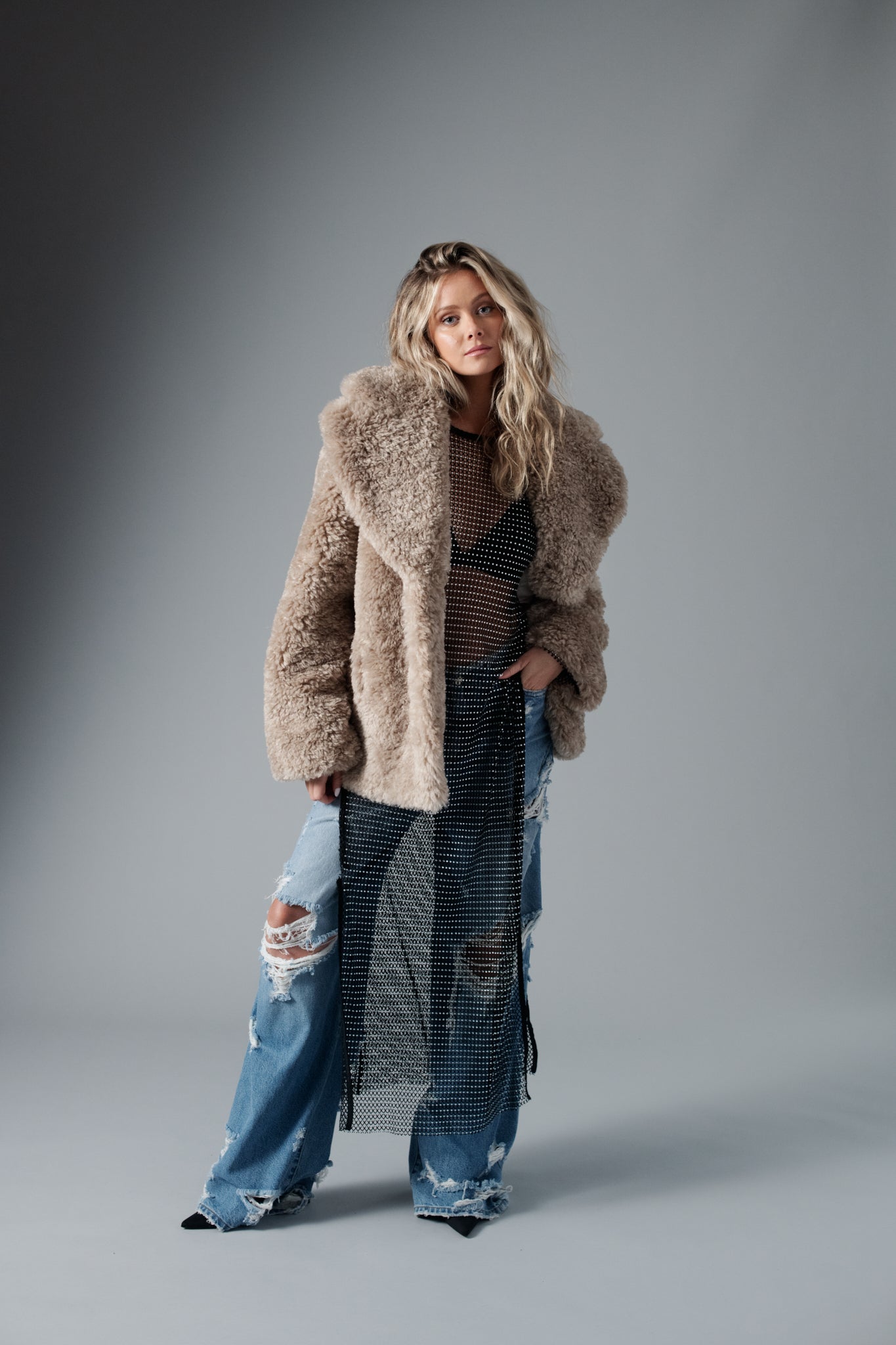 Hannah Godwin wearing beige faux fur coat, mesh see-through dress, destruction denim jeans by Avec Les Filles women's fashion clothing